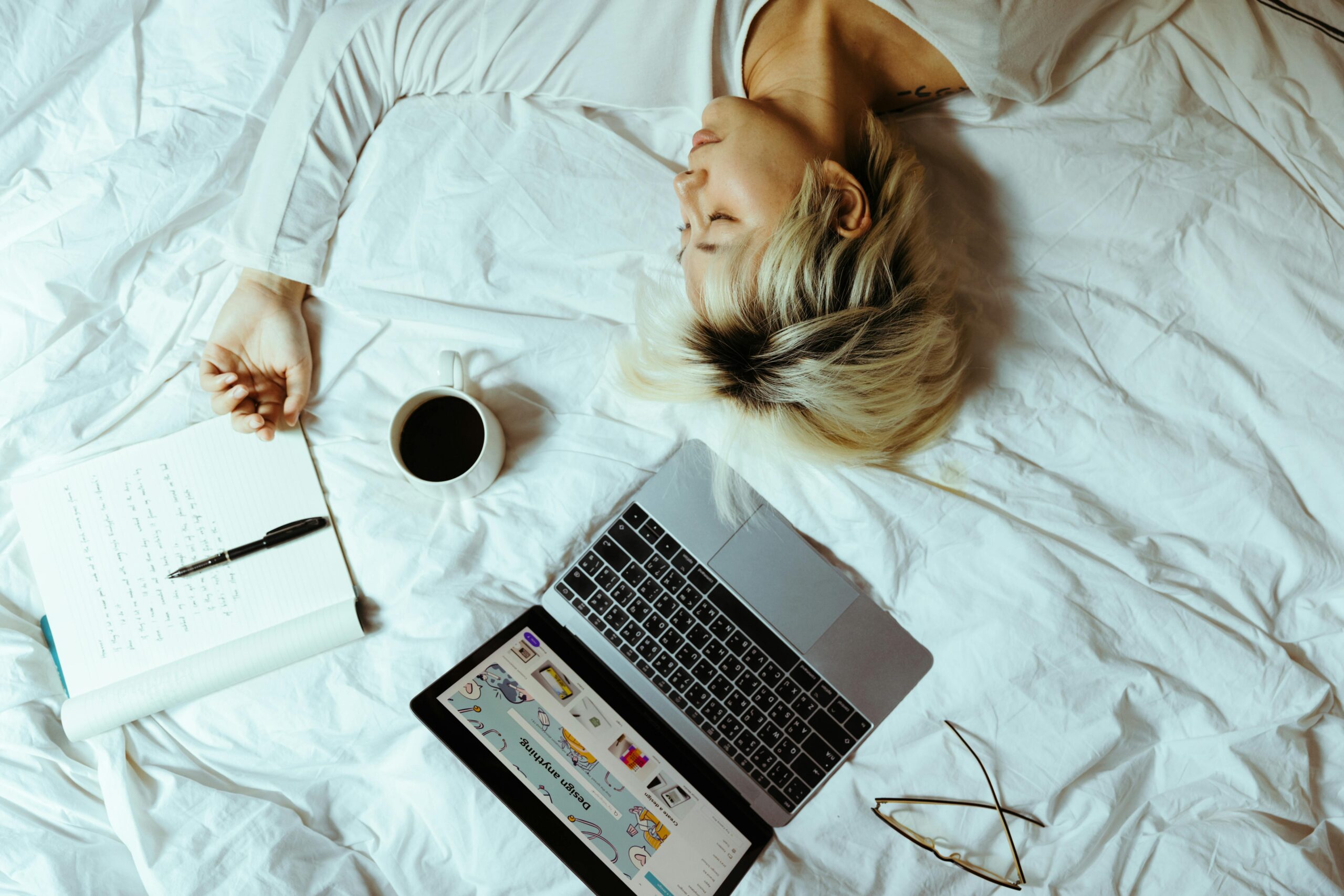 Primer prokrastinacije, devojka leži na krevetu sa laptopom i kafom